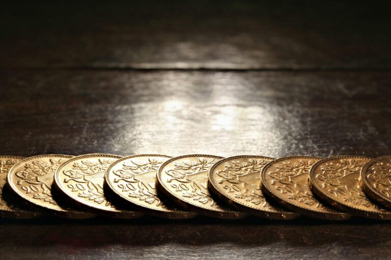 Row of gold-colored coins lined up on a dark wooden surface, reflecting light.
